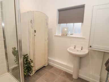A bathroom with a shower, a corner cabinet, a pedestal sink, and a window with a blind at Cheviot View in Crookham near Cornhill-On-Tweed
