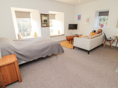 A bedroom with a bed a sofa a wall-mounted TV and two windows with seats at Cheviot View in Crookham near Cornhill-On-Tweed