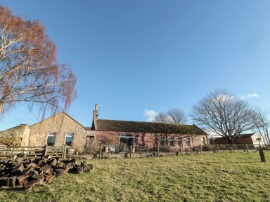 A stone and brick house with a fenced yard and chopped wood under trees at Cheviot View in Crookham near Cornhill-On-Tweed