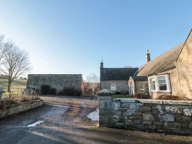 A courtyard with stone buildings trees and a gravel driveway at Cheviot View in Crookham near Cornhill-On-Tweed