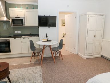 A kitchen and dining area with a round table and two chairs a wall-mounted television a white cupboard and an open door at Flodden in Crookham near Cornhill-On-Tweed
