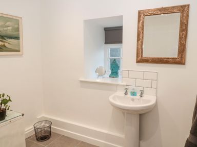 A bathroom with a pedestal sink a mirror a small window with a blind a wastebasket plant and a painting at Flodden in Crookham near Cornhill-On-Tweed