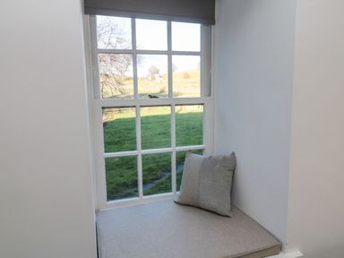 A window with a gray cushion and pillow on the sill overlooking a green field at Flodden in Crookham near Cornhill-On-Tweed