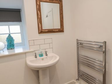 A bathroom with a white pedestal sink, a mirror with a decorative frame, a towel radiator, and a window with a blue Buddha statue on the sill at Flodden in Crookham near Cornhill-On-Tweed