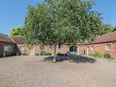 A gravel courtyard with a tree in the center surrounded by single-story brick buildings at Flodden in Crookham near Cornhill-On-Tweed