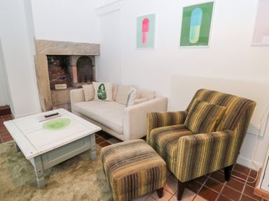 A seating area with a cream sofa and striped armchair next to a stone fireplace at Bakers Cottage in Crookham near Cornhill-On-Tweed