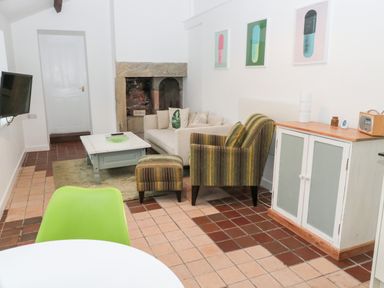 A living room with a beige sofa striped armchair coffee table and television at Bakers Cottage Crookham near Cornhill-On-Tweed