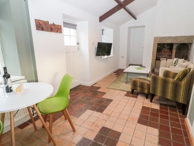 A living room with a round white table and green chairs a wall-mounted TV and a seating area with striped and plain sofas at Bakers Cottage in Crookham near Cornhill-On-Tweed