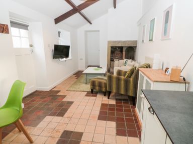 A sitting area with striped armchair and ottoman a beige sofa a coffee table and a fireplace at Bakers Cottage Crookham near Cornhill-On-Tweed