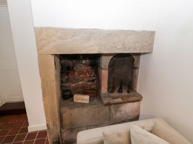 A stone fireplace with vintage irons and tools inside the hearth at Bakers Cottage in Crookham near Cornhill-On-Tweed