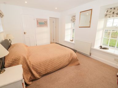 A bedroom with a double bed covered in a tan quilt next to two windows with bird patterned blinds at Bakers Cottage in Crookham near Cornhill-On-Tweed