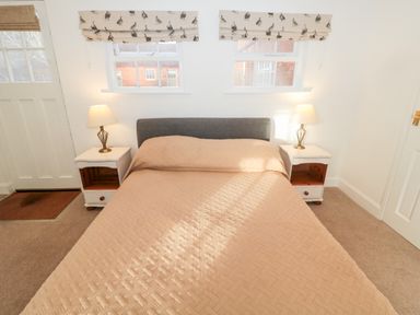 A bedroom with a double bed two bedside tables with lamps and two windows with printed blinds at Bakers Cottage Crookham near Cornhill-On-Tweed