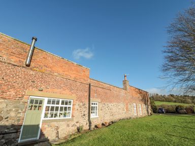A brick and stone cottage with windows and a green door on a grassy lawn with cars and trees at Bakers Cottage Crookham near Cornhill-On-Tweed