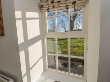 A window with divided panes showing green grass and bare trees outside at Bakers Cottage Crookham near Cornhill-On-Tweed
