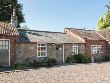 A stone and brick cottage with green doors and windows a bench and plants outside at Bakers Cottage in Crookham near Cornhill-On-Tweed