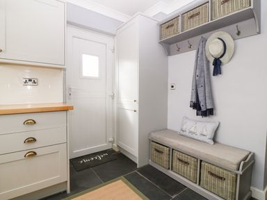 A small entryway with a white door a bench with baskets hooks with a hat and scarf and kitchen cabinets at Valley Pines in Valley