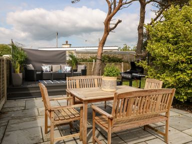 A patio with a wooden table and chairs a plant on the table a bbq grill a raised seating area with outdoor sofas and cushions and plants at Valley Pines in Valley
