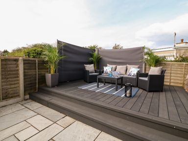 An outdoor seating area with a black couch and two chairs around a coffee table on a wooden deck at Valley Pines in Valley