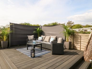An outdoor patio area with black wicker seating set including a sofa and chairs a table a striped rug potted plants and privacy screens at Valley Pines in Valley