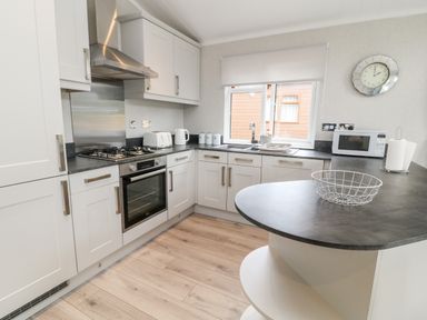 A kitchen with white cabinets a gas stove an oven a microwave and a window with a roller blind at Woodpecker Lodge in Highampton near Sheepwash