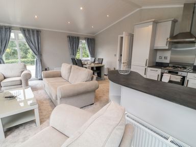 An open living room and kitchen with beige sofas dining table and kitchen appliances at Woodpecker Lodge in Highampton near Sheepwash