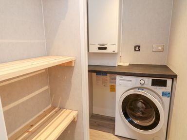 A utility room with a washing machine wooden shelves and a boiler at Woodpecker Lodge in Highampton near Sheepwash