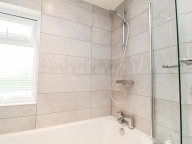 A bathroom with bathtub shower fixtures tiled walls and a window at Woodpecker Lodge in Highampton near Sheepwash