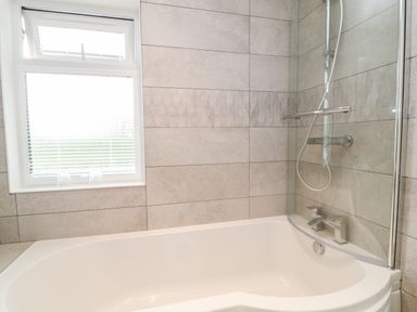 A bathroom with a bathtub shower combination and a window with blinds at Woodpecker Lodge in Highampton near Sheepwash