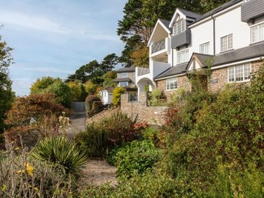 A residential building with white walls and stone accents surrounded by bushes and trees at 14 St Elmo Court in Salcombe