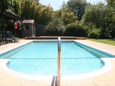 An outdoor swimming pool with blue tile lining surrounded by a patio with lounge chairs a shed and trees in the background at 14 St Elmo Court in Salcombe