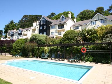 An outdoor swimming pool with chairs and a life buoy in front of multi-story residential buildings at 14 St Elmo Court in Salcombe