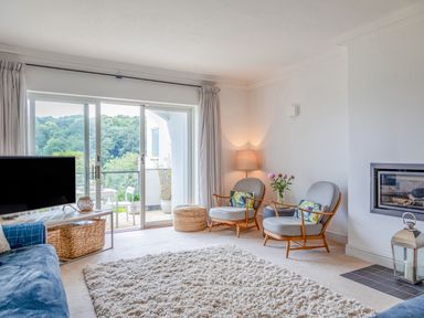 A living room with two chairs a lamp a fireplace and sliding glass doors leading to a balcony at 14 St Elmo Court in Salcombe