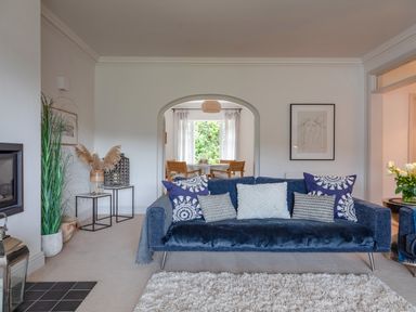 A living room with a blue sofa and cushions a white rug and a dining area through an arch at 14 St Elmo Court in Salcombe