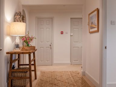 A hallway with a wooden table holding a lamp and flowers two closed doors and a framed picture on the wall at 14 St Elmo Court in Salcombe