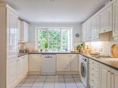A kitchen with white cabinets a window above the sink a dishwasher and a washing machine at 14 St Elmo Court in Salcombe