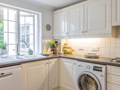 A kitchen with white cabinets a washing machine a sink and kitchen utensils at 14 St Elmo Court in Salcombe