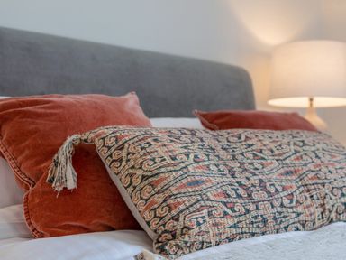 A bed with a gray headboard, patterned pillow, two red pillows, and a lamp in the background at 14 St Elmo Court in Salcombe