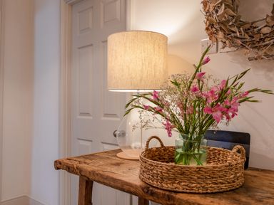 A wooden table with a lamp and a basket holding a vase of pink flowers at 14 St Elmo Court in Salcombe
