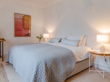 A bedroom with a bed covered with a quilt and pillows beside nightstands with lamps at 14 St Elmo Court in Salcombe