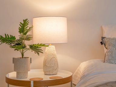 A bedside table with a potted plant and a lamp next to a bed at 14 St Elmo Court in Salcombe