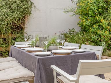 An outdoor dining table set with white plates wine glasses and potted plants surrounded by white chairs and greenery at 14 St Elmo Court in Salcombe