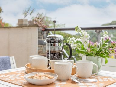 A table set with white mugs a French press a plate of biscuits and a vase of flowers at 14 St Elmo Court in Salcombe