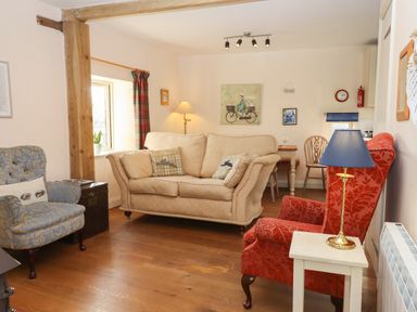 A living room with three armchairs one beige one red and one blue wooden floor and a small table with a lamp at The Old Dairy in Colyton