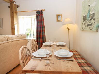 A dining table with plates and glasses next to a window and sofa at The Old Dairy in Colyton