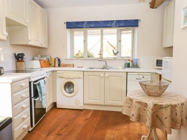 A kitchen with white cabinets appliances and a small table with a cloth at The Old Dairy in Colyton