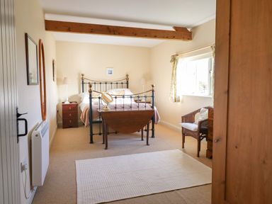 A bedroom with a metal bed frame bedside tables a wicker chair and a window at The Old Dairy in Colyton