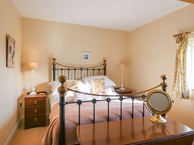 A bedroom with a metal bed frame two bedside tables with lamps and a mirror on a wooden dresser at The Old Dairy in Colyton
