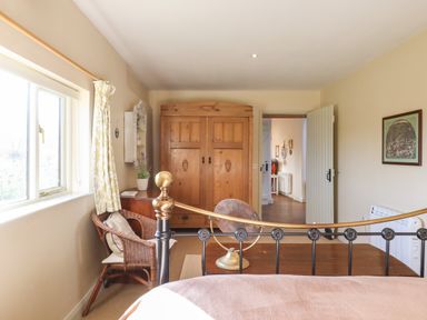 A bedroom with a metal bed frame a wooden wardrobe a wicker chair and a window with patterned curtains at The Old Dairy in Colyton