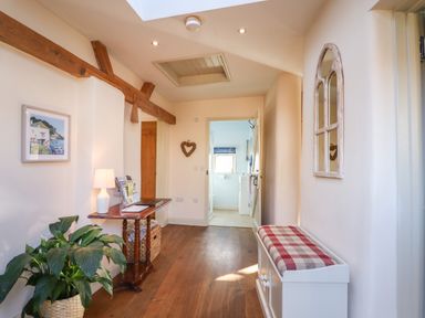 A hallway with wooden floor a small table with a lamp and plant a bench with a cushion and a wall mirror at The Old Dairy in Colyton