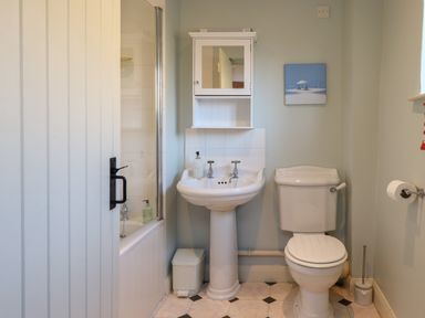 A bathroom with a toilet sink cabinet bathtub and a small trash bin at The Old Dairy in Colyton